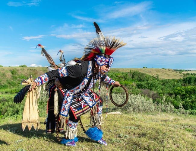 An Indigenous man dancing outside dressed in traditional beaded clothing