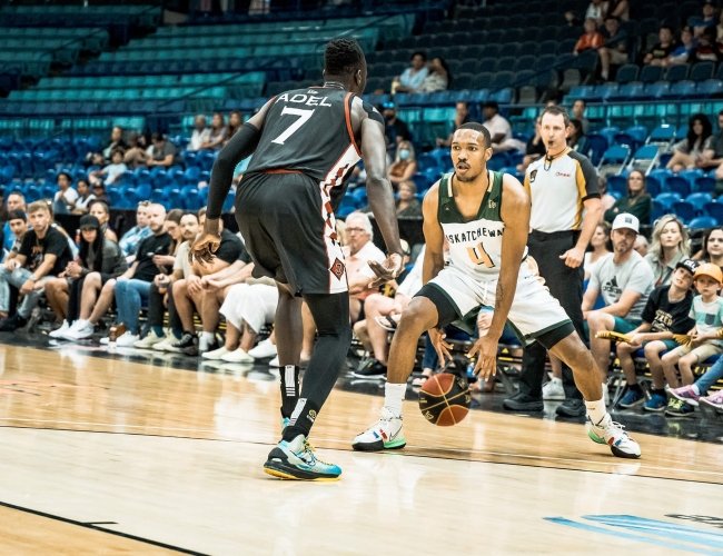 Two players in a professional basketball game. One man in dribbling a basketball.