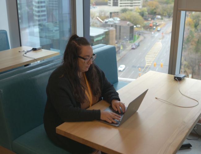 woman working on her laptop at a bench seating area at 7 Shifts