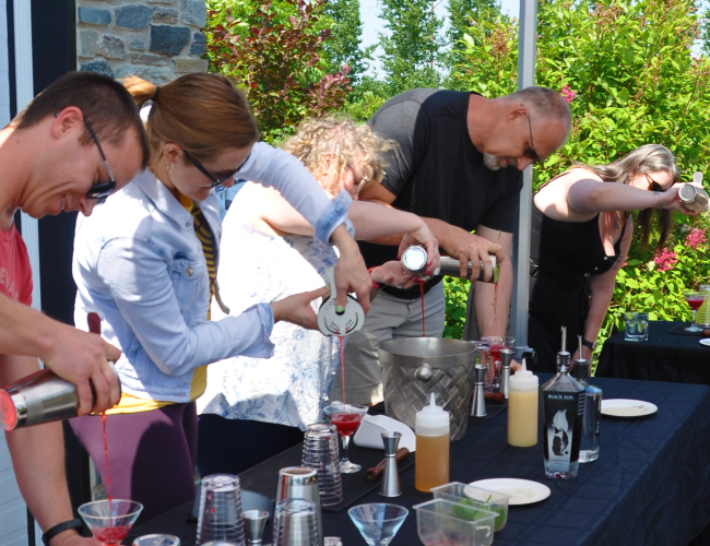 Five individuals outside pouring cocktails into a glass that they made during a Cocktail Class