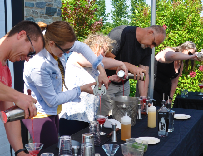 Five individuals outside pouring cocktails into a glass that they made during a Cocktail Class