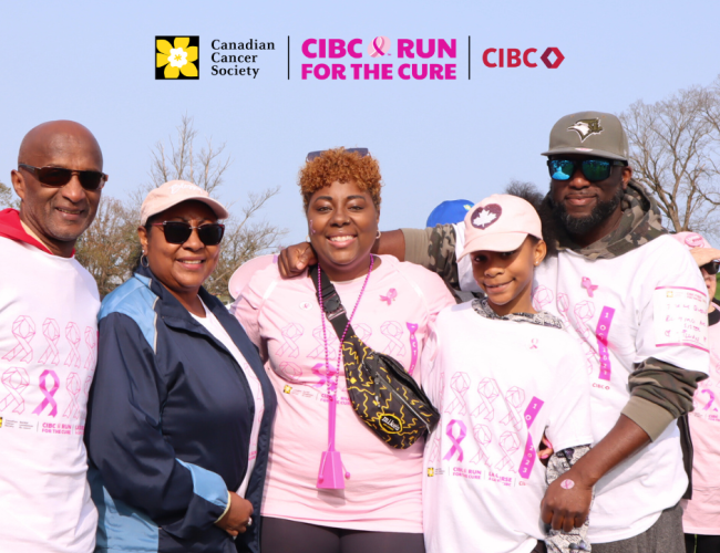 Four adults and one child, all wearing pink shirts, smile at the camera