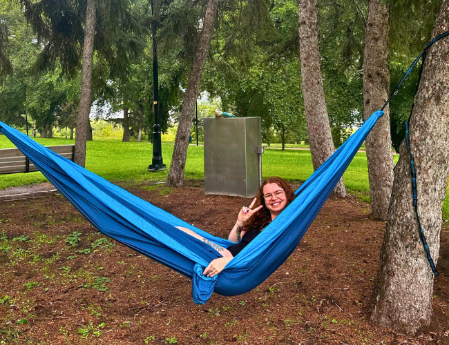 Redheaded person sitting in a hammock holding up the peace sign