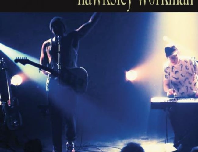 Image of Hawksley Workman on the left side with light only shining on guitar. Pianist on right side. Sponsor logos in bottom left and text saying: "Tickets available at broadwaytheatre.ca or at the broadway" in the left corner. Other text says october 23rd at 7:30pm at the roxy theatre. 