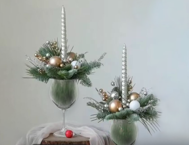 Two centerpieces made with a wine glass, fresh greenery, and festive ornaments.