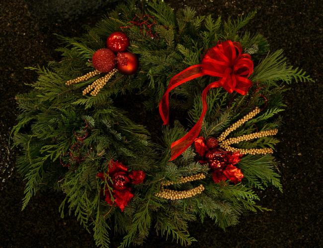 Traditional holiday wreath made from fresh greenery, red and gold festive ornaments.