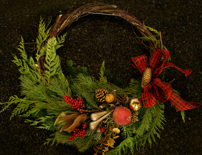 Vine wreath made with fresh greenery, red and gold ornaments as decoration.