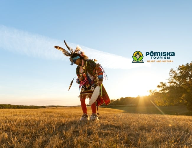 Indigenous dancer in regalia in a field with a sunny golden hour background