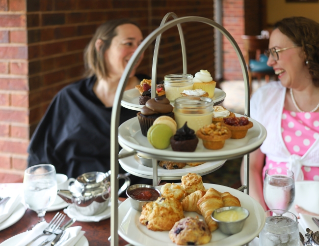 Two women laughing behind serving plates filled with pastries and desserts