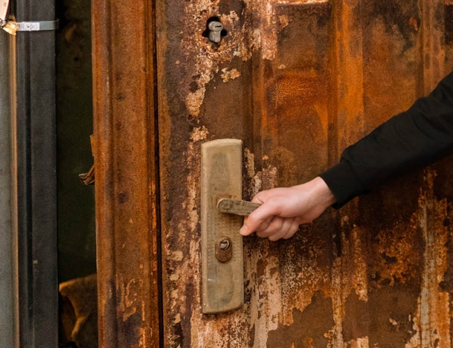 a hand turning a door handle and opening a damaged brown door