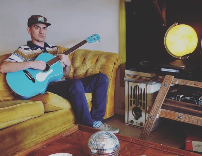 Wax playing guitar on a yellow couch