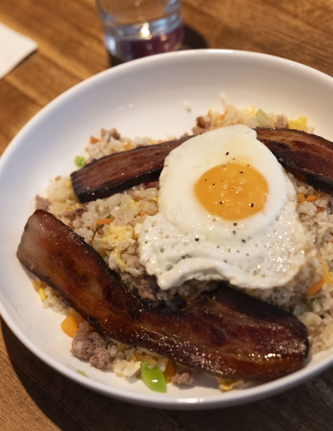 A bowl of rice topped with crispy bacon and sunny-side-up eggs