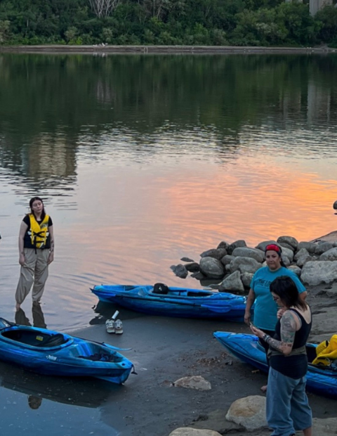 6 people standing along the river with kayaks and life jackets