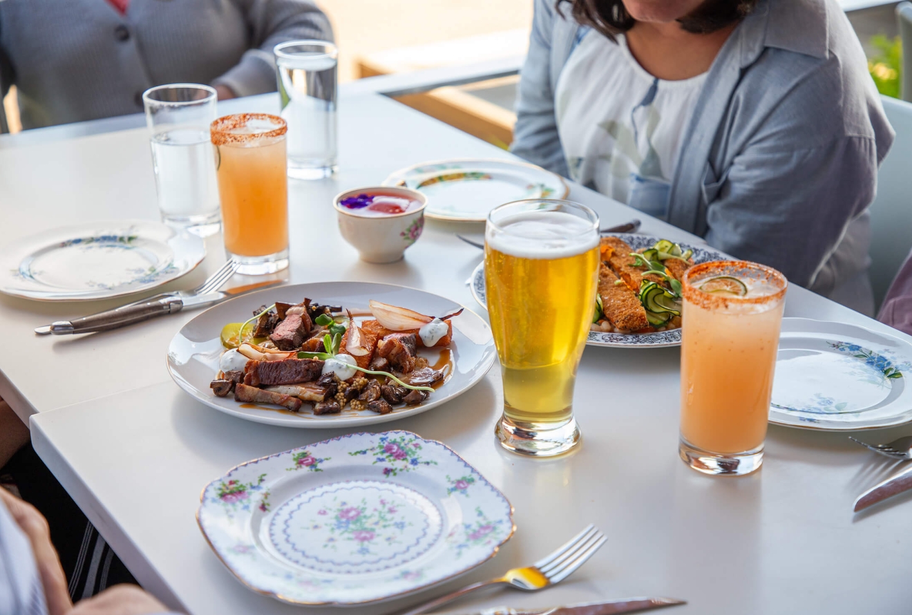 An outdoor restaurant table set with appetizers and cocktail/beer drinks